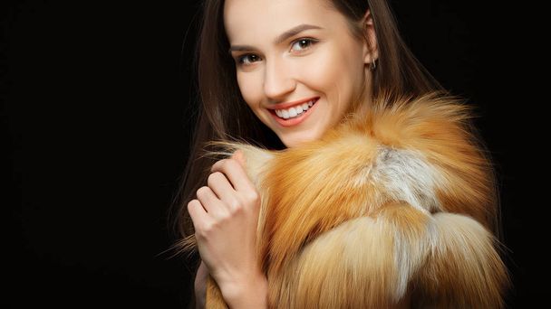 Portrait of beautiful happy girl with natural makeup in fluffy fur coat on black background - Zdjęcie, obraz