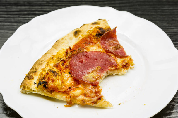 A bitten portion of pepperoni pizza on a plate. - Photo, Image