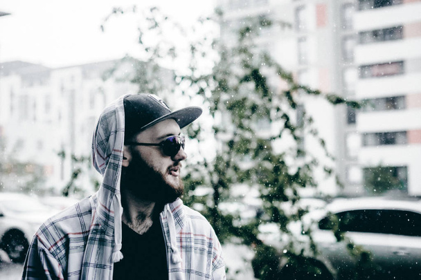 young man with beard in light checkered jacket with hood walking freely around city - Foto, immagini