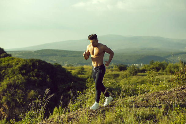 Handsome strong muscular athletic man working out and running outdoors in nature - Photo, Image