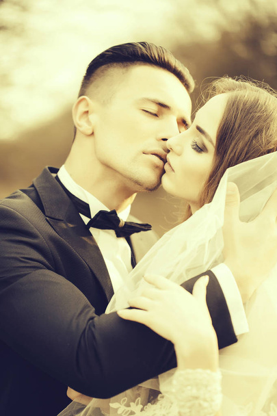 Beautiful bridal couple of young man embracing and kissing pretty woman outdoor - Fotografie, Obrázek