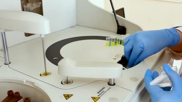 A rapariga num laboratório médico coloca as amostras de soro na máquina para análise. Equipamento, análise bioquímica automática. Lá dentro. Reagentes coloridos. A câmera está fixa
 - Filmagem, Vídeo