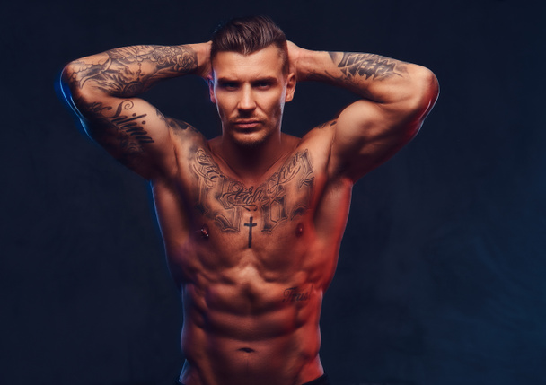 Un hombre musculoso tatuado sobre un fondo oscuro
. - Foto, imagen