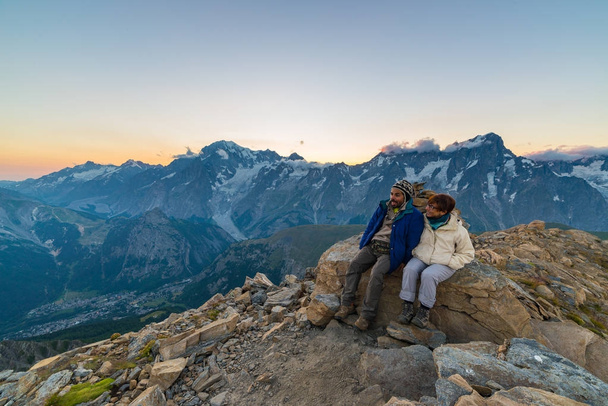Couple of people looking at the sunrise over Mont Blanc mountain peak (4810 m). Valle d'Aosta, italian summer adventures and travel destination on the Alps. - Photo, Image