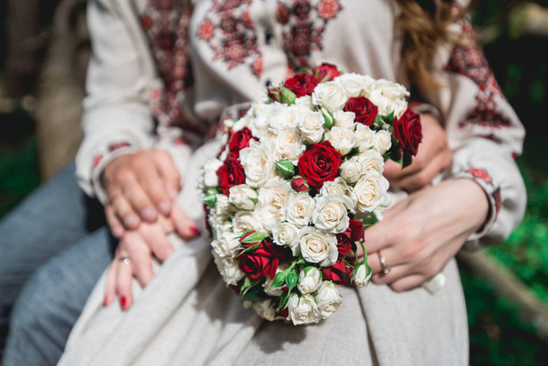 verloofde en de bruid in de hand te houden bruiloft boeket biege en rode rozen. - Foto, afbeelding