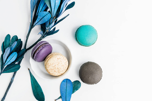 Top view flat lay colorful macarons and blue leaves on white table. Creative dessert concept - Foto, Imagen