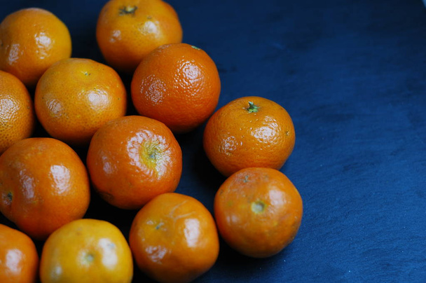 Unpeeled mandarins on a dark background with hard light. - Zdjęcie, obraz