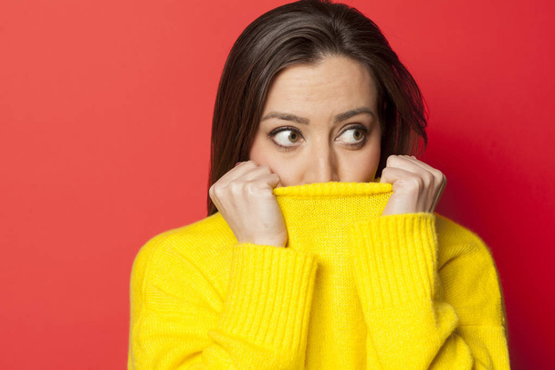Όμορφη γυναίκα φοβάται σε κίτρινο πουλόβερ σε κόκκινο φόντο - Φωτογραφία, εικόνα