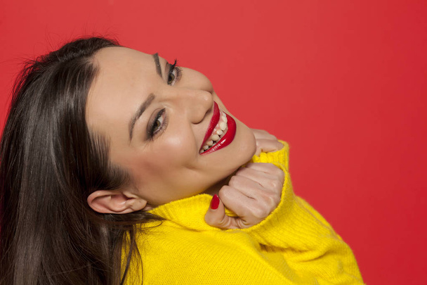 赤い背景の上の黄色のセーターに美しい幸せな女 - 写真・画像