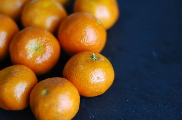 Unpeeled mandarins on a dark background with hard light. - Zdjęcie, obraz
