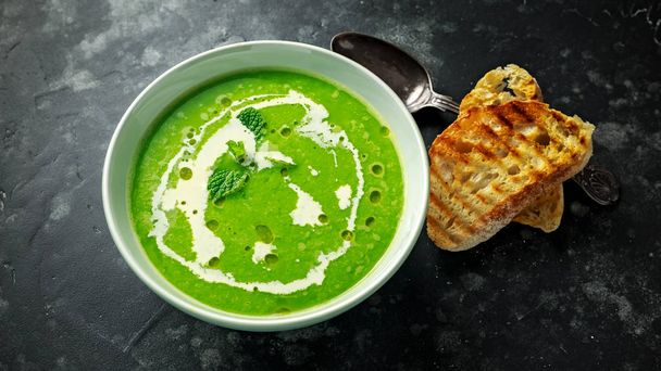 Green sweet pea and mint soup with cream and olive oil drizzle served with grilled ciabatta toasts - Photo, Image