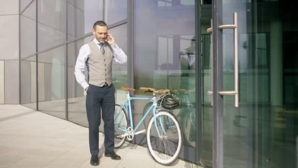 4K Businessman with bicycle leaving office building and talking on cell phone - Materiał filmowy, wideo