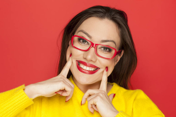 Beautiful happy woman with red frame glasses on a red background - Photo, Image
