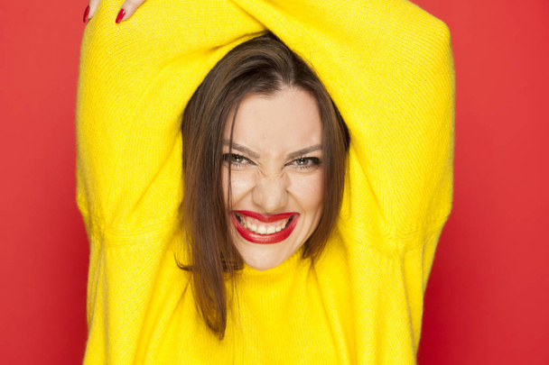 Όμορφη σέξι γυναίκα στον κίτρινο μπλούζα που δείχνει τα δόντια της σε κόκκινο φόντο - Φωτογραφία, εικόνα