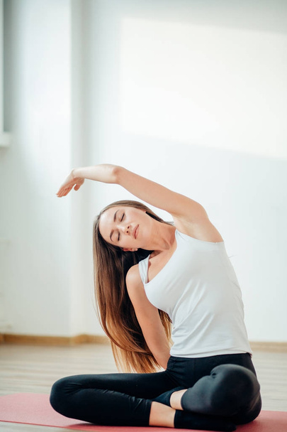 Young slim girl makes aerobics exercise sitting in lotus pose on mat - Фото, изображение