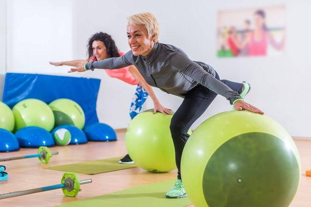 Fit mulheres caucasianas fazendo exercício guindaste em pé em uma perna com os braços para fora para os lados segurando para equilibrar a bola durante o treinamento em clube de fitness
 - Foto, Imagem