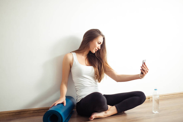 woman sitting on floor and making selfie on smartphone in fitness gym - Foto, imagen