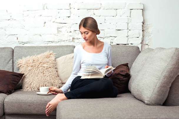 Woman reading a book on sofa - Фото, изображение