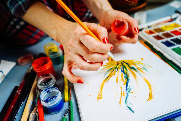 woman artist paints with a brush and bright watercolor paints on white paper - Fotó, kép