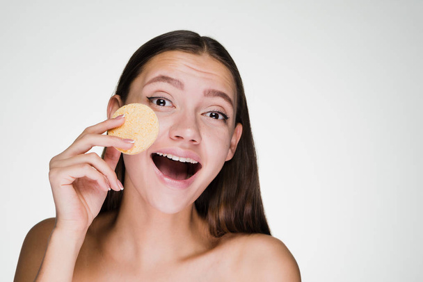 happy young girl holding a sponge for cleansing the skin on her face - Foto, Imagen
