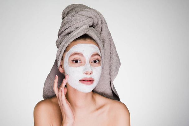 young attractive girl with a towel on her head applied a white moisturizing mask on her face - Photo, Image