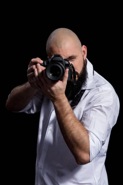 Fotograaf met de camera. Mannelijke fotograaf met baard in een wit overhemd foton overname met zwarte achtergrond - Foto, afbeelding