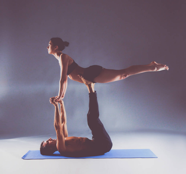 Young couple practicing acro yoga on mat in studio together - 写真・画像