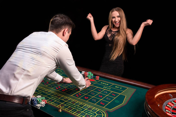 Zbliżenie na odwrocie krupier w białej koszuli, obraz zielony kasyno tabeli z ruletka i żetony, bogate kobiety zakładów hazardowych w tle - Zdjęcie, obraz