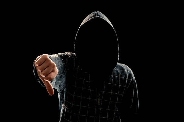 Silhouette of a man in a hood on a black background, his face is not visible, showing a fist in the camera. The concept of a criminal, incognito, mystery, secrecy, anonymity. - Foto, afbeelding