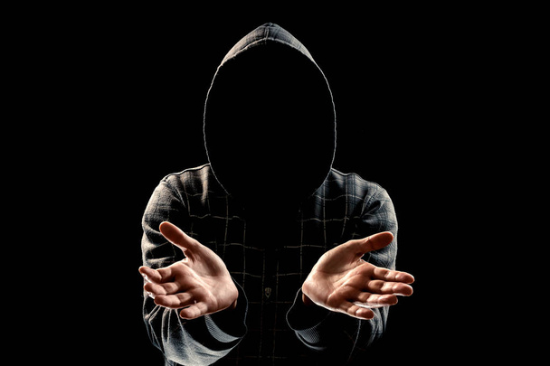 Silhouette eines Mannes mit Kapuze auf schwarzem Hintergrund, das Gesicht ist nicht zu sehen, zeigt die Handflächen in die Kamera. das Konzept eines Verbrechers, Inkognito, Mysteriums, Geheimhaltung, Anonymität. - Foto, Bild