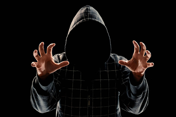 Silhouette of a man in a hood on a black background, his face is not visible, trying to attack. The concept of a criminal, incognito, mystery, secrecy, anonymity. - Foto, immagini