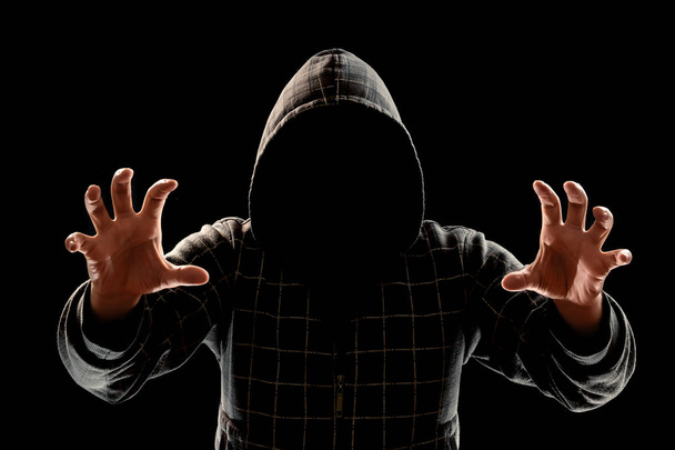 Silhouette di un uomo in un cappuccio su uno sfondo nero, il suo volto non è visibile, cercando di attaccare. Il concetto di criminale, in incognito, mistero, segretezza, anonimato
. - Foto, immagini