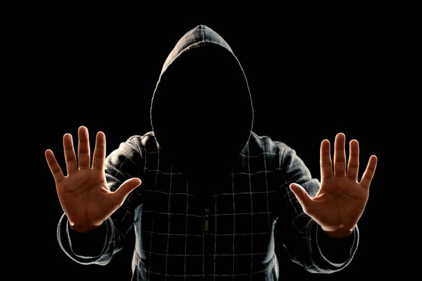 La silueta de un hombre en una capucha sobre un fondo negro, la cara no es visible, muestra las palmas en la cámara. El concepto de un criminal, de incógnito, misterio, secreto, anonimato
. - Foto, imagen