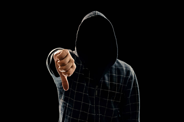 Silhouet van een man in een capuchon op een zwarte achtergrond, zijn gezicht is niet zichtbaar, een vuist in de camera te tonen. Het concept van een misdadiger, incognito, mysterie, geheimhouding, anonimiteit. - Foto, afbeelding