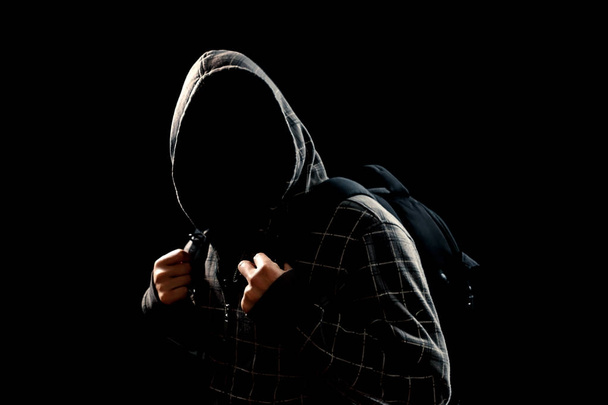 Silhouette of a man in a hood on a black background, his face is not visible, behind his backpack. The concept of a criminal, incognito, mystery, secrecy, anonymity. - Foto, imagen