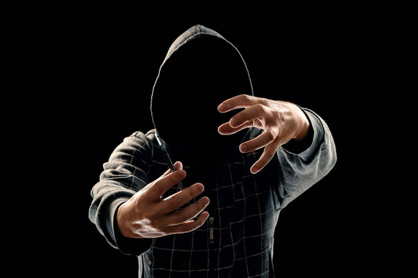 Silhouette of a man in a hood on a black background, his face is not visible, the hacker is holding the phone in his hands. The concept of a criminal, incognito, mystery, secrecy, anonymity. - Valokuva, kuva