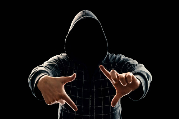 Silhouette eines Mannes mit Kapuze auf schwarzem Hintergrund, sein Gesicht ist nicht sichtbar, etwas, das seine Hände zeigt. das Konzept eines Verbrechers, Inkognito, Mysteriums, Geheimhaltung, Anonymität. - Foto, Bild
