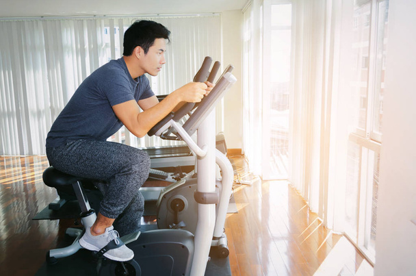 muscular young asian man exercising his legs cardio training on bicycle in fitness gym for good healthy at the morning, bodybuilder, lifestyle, exercise fitness, workout and sport training concept - Photo, Image