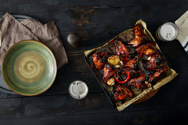 Top view baked chicken wings in soy sauce with honey on dark wooden table with beer. Dinner table concept - 写真・画像