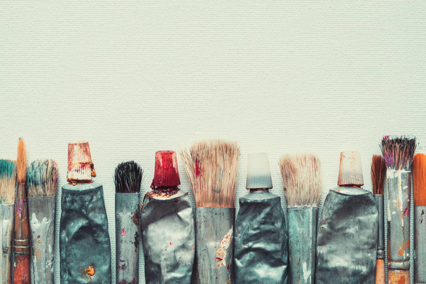 Row of artist paintbrushes and paint tubes closeup on artistic canvas background, retro stylized. Copy space for text. - Foto, Bild
