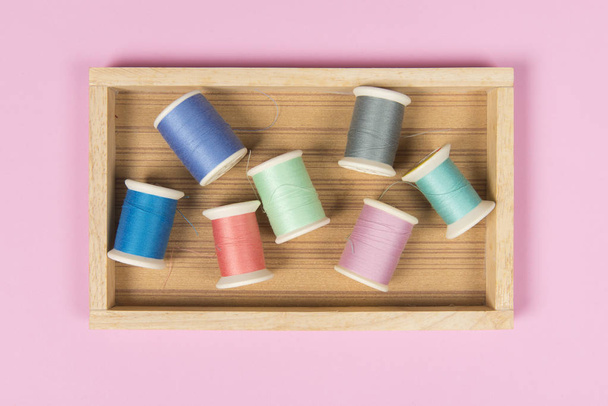 Flat lay of colored thread rolls for sewing on pink background,  - Фото, изображение