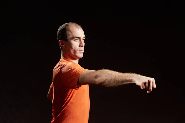 Взрослый мужчина тренирует удар рукой на черном фоне
 - Фото, изображение