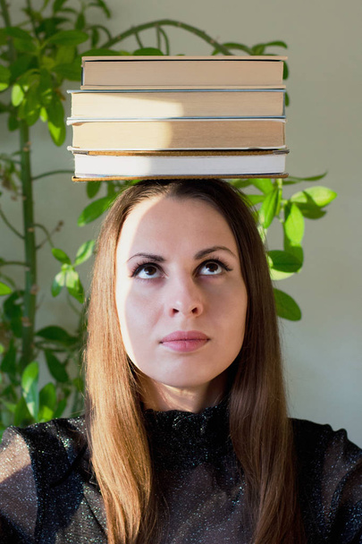 girl with books on head looks up - Фото, изображение