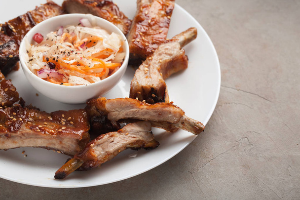 Gegrilde varkensribbetjes in barbecue saus en honing met zuurkool op wit bord. Snack tot bier op een stenen Lichttafel - Foto, afbeelding