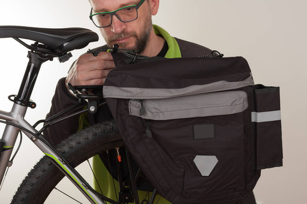 Бородатый человек вставляет сумку с велосипедом на заднюю стойку велосипеда MTB
 - Фото, изображение