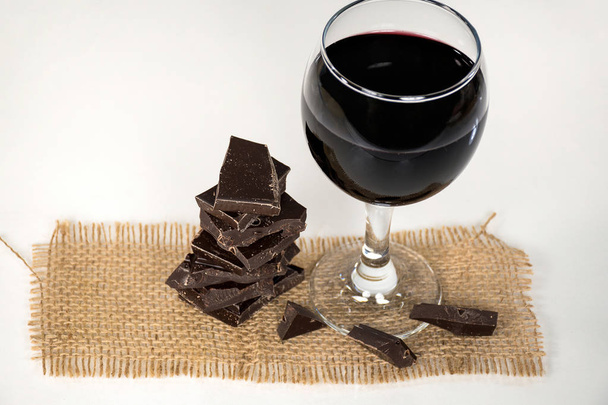 red wine in stemware with dark chocolate candy on brown burlap - Foto, Bild
