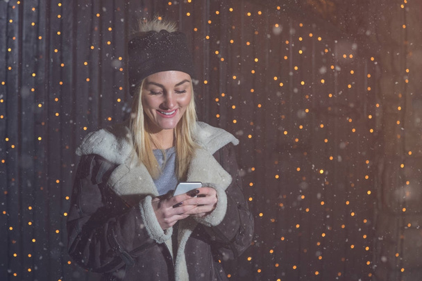 Young woman using smart phone next to Christmas lights on the st - Foto, imagen