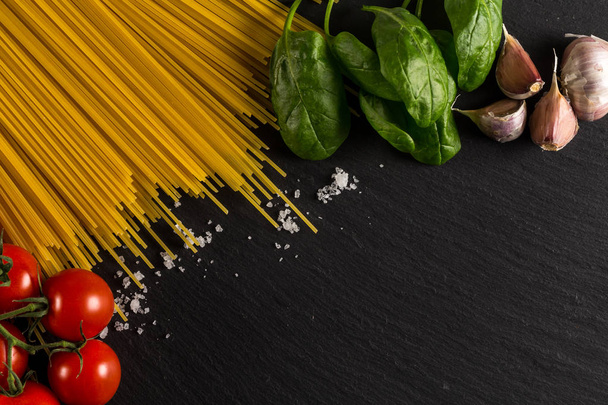 Food frame photo. Pasta ingredients. Cherry-tomatoes, spaghetti pasta, garlic, basil, salt  on dark grunge backdrop, copy space, top view, horizontal - Foto, Imagen