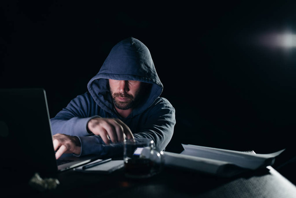 adam hacker bir ceket ile bir kukuleta ile bir dizüstü bilgisayar oturuyor - Fotoğraf, Görsel
