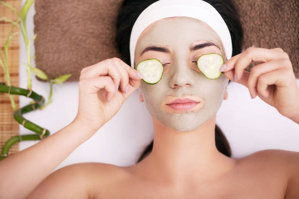Beautiful young woman is getting facial clay mask at spa, lying  - Foto, Imagem